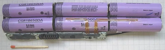 An opened battery pack showing cylindrical CGR18650DA cells wired together, with a match beside them for scale.